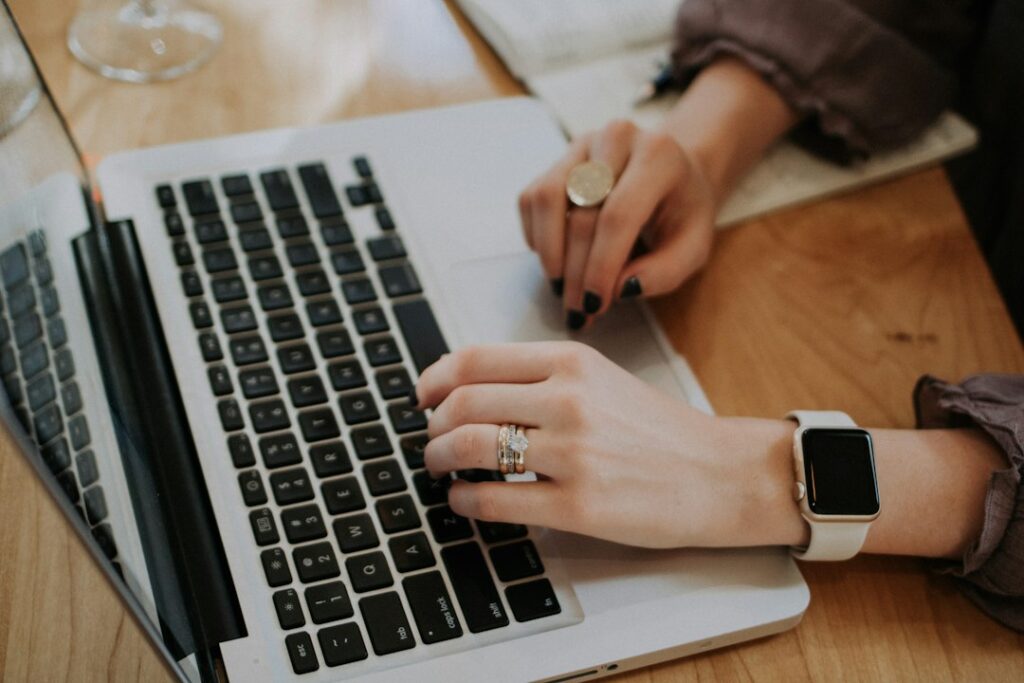 Hands using a laptop keyboard and trackpad on a wooden table.
