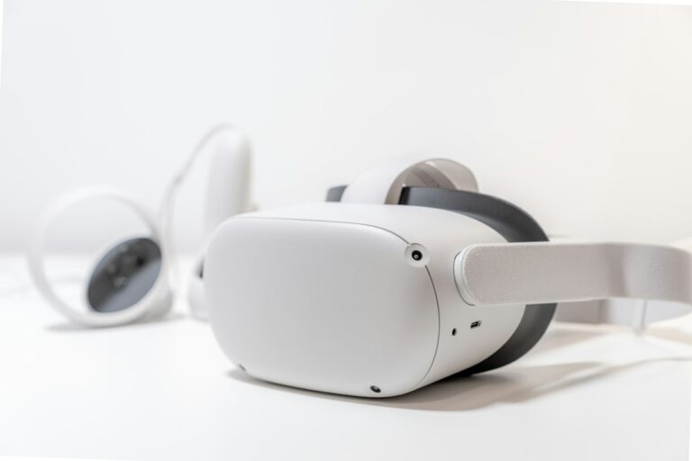 A white virtual reality headset and controllers resting on a white desk.
