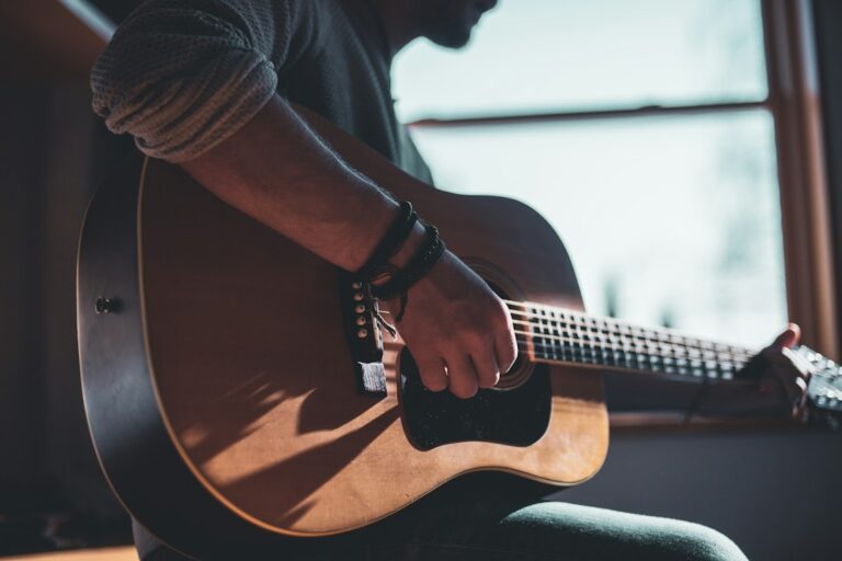 A person playing an acoustic guitar beside a window.
