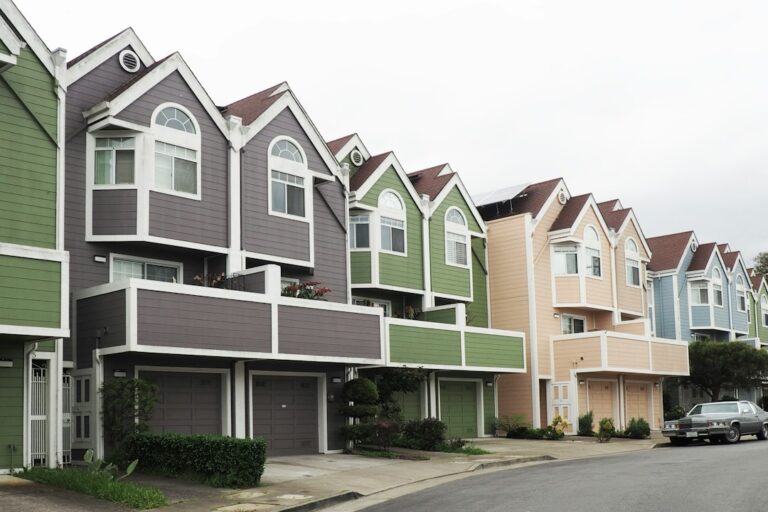 A row of pastel-colored houses with garages beside a residential street.