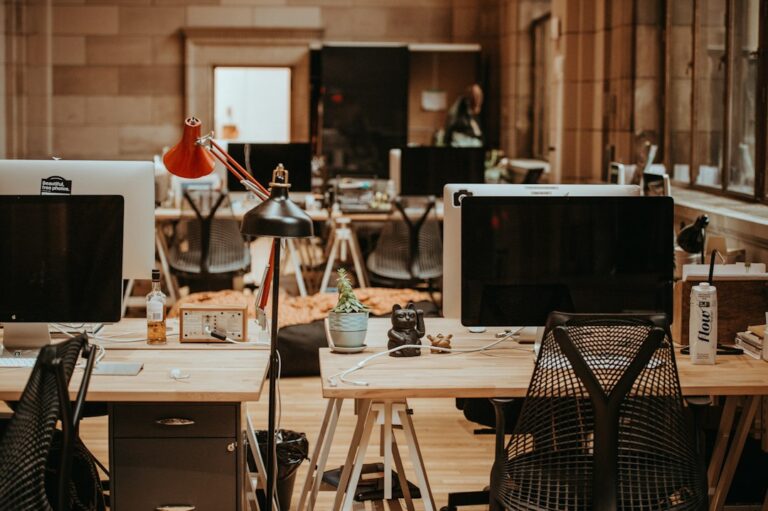 Computer monitors, lamps, and office chairs arranged around shared wooden desks.
