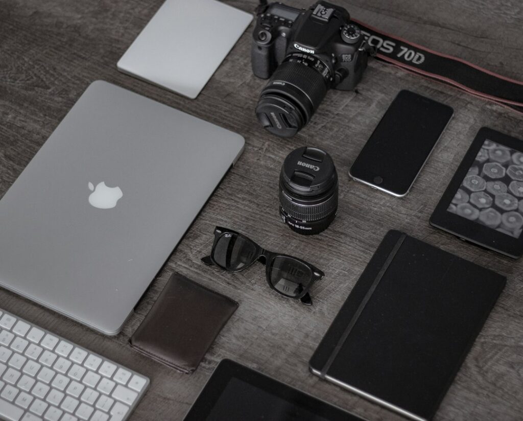 Camera, lenses, laptop, phone and notebook arranged on a wooden desk