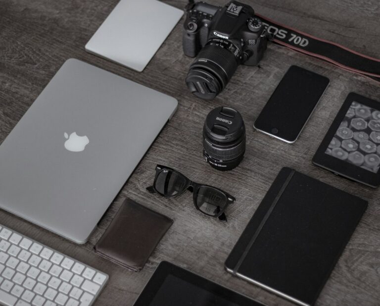 Camera, lenses, laptop, phone and notebook arranged on a wooden desk