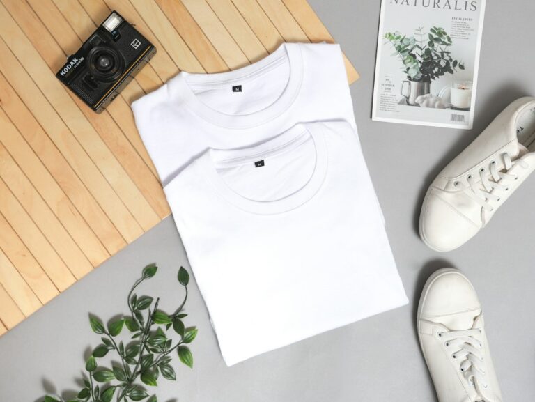 Two folded white T-shirts beside sneakers, a camera and a plant.