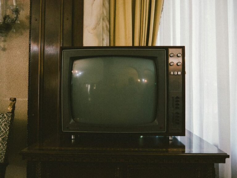 Vintage television with a dark screen on a wooden cabinet beside a curtained window.
