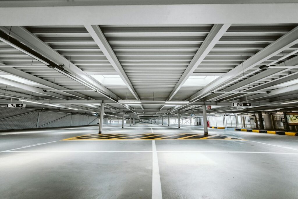 A bright, empty parking garage with marked lanes, steel beams and signs for lifts.