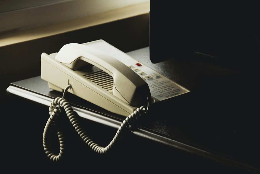 A cream-colored corded telephone on a dark desk beside a monitor.