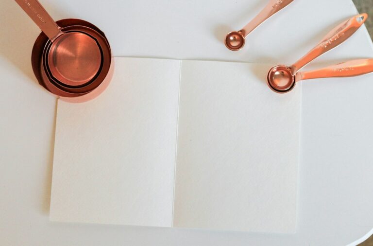 Copper-colored measuring cups and spoons beside a blank sheet of paper.