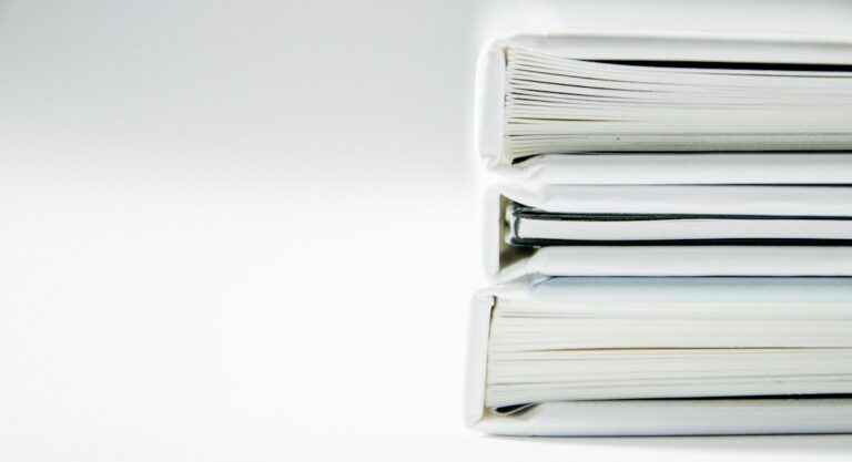 Three white-covered volumes stacked on a white surface.