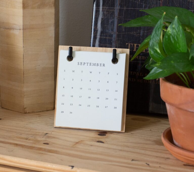 A small paper calendar on a wooden shelf beside a potted plant.