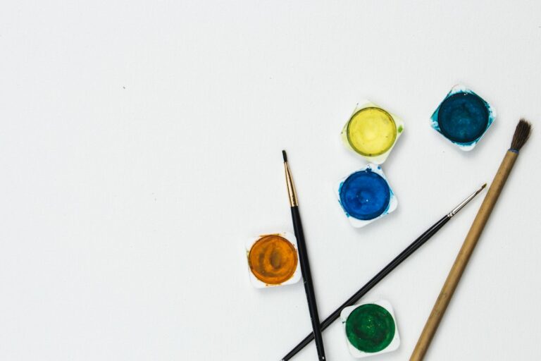 Paintbrushes and small pots of watercolor paint on a white surface.