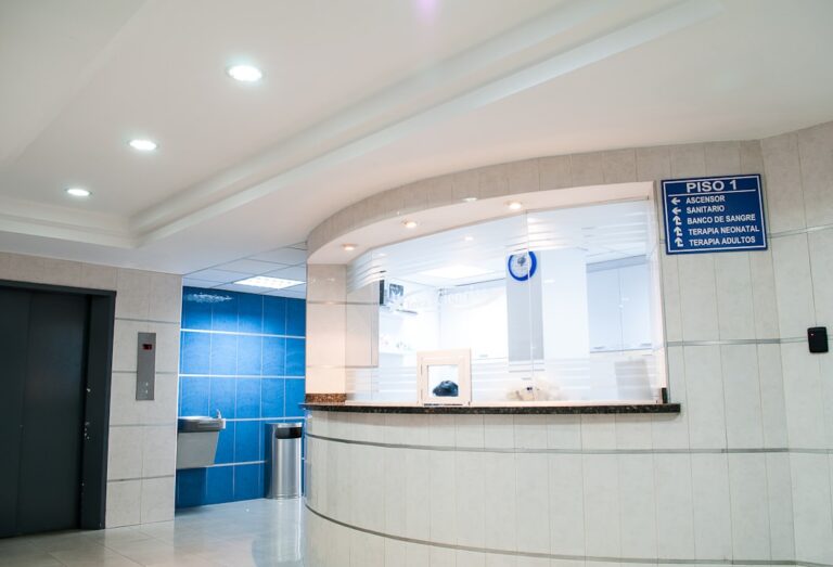 A hospital reception window beside an elevator and directional signs.