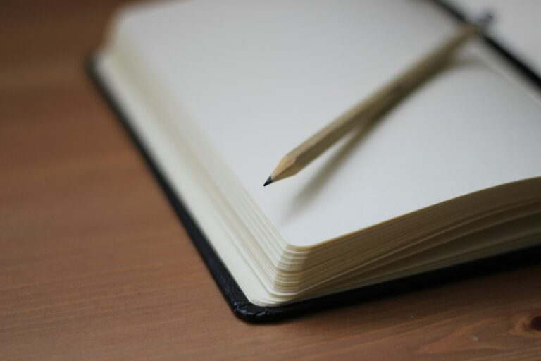A pencil resting diagonally across an open notebook on a wooden table.