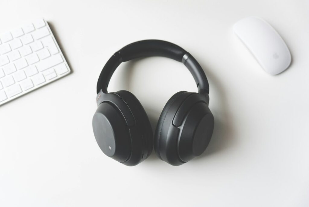 Black headphones between a white keyboard and mouse on a desk.