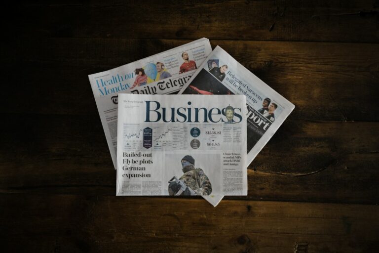 Business and other newspaper sections arranged on a dark wooden table.