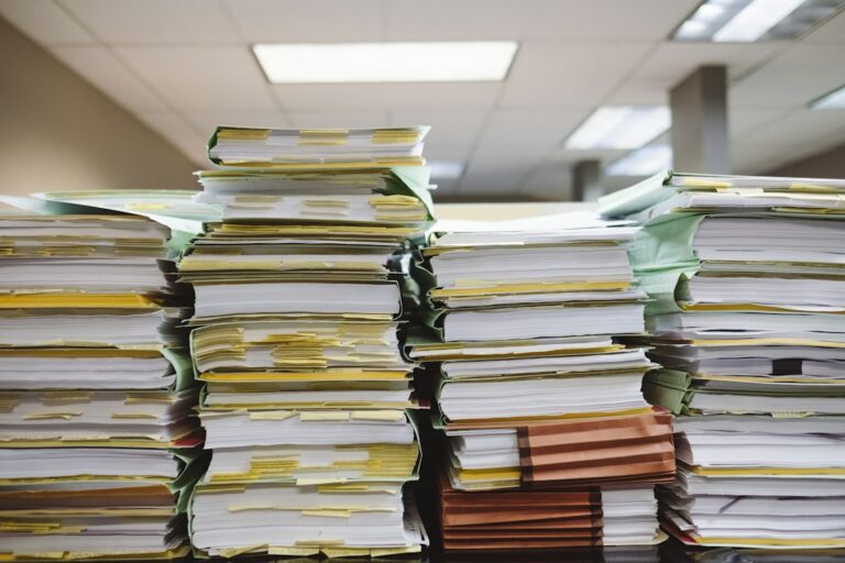 Stacks of paper files and folders on an office surface.