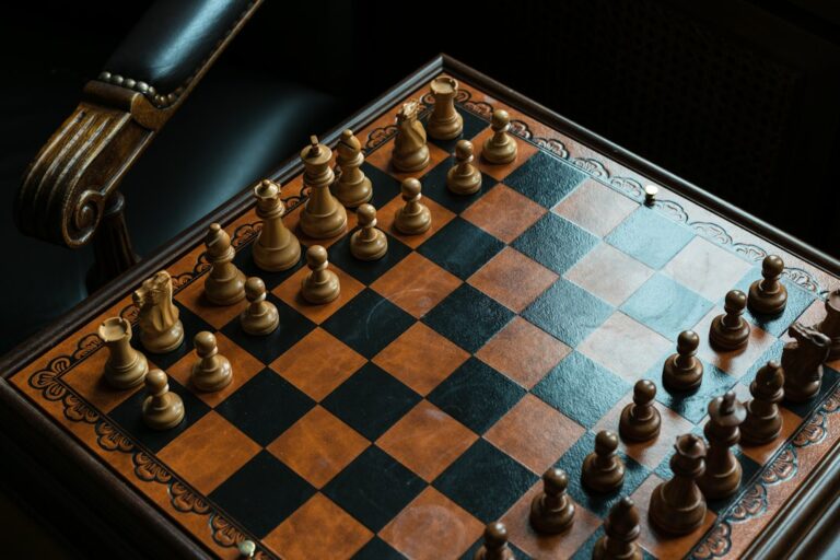Wooden chess pieces arranged on a chessboard beside a leather chair.