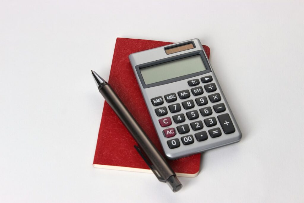 A calculator and black pen resting on a red notebook.