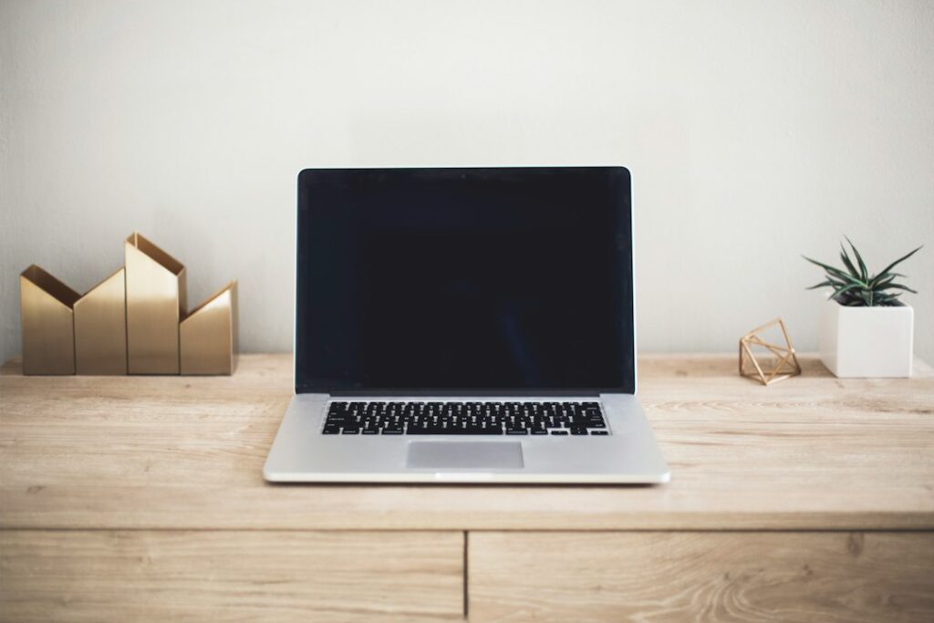 An open laptop with a dark screen beside a small plant on a wooden desk.