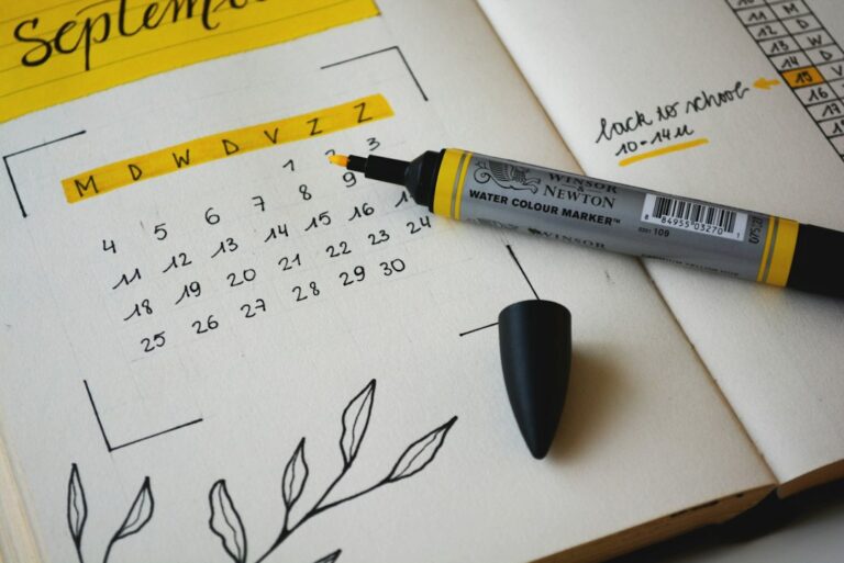 Open notebook with a handwritten monthly calendar and a yellow marker.
