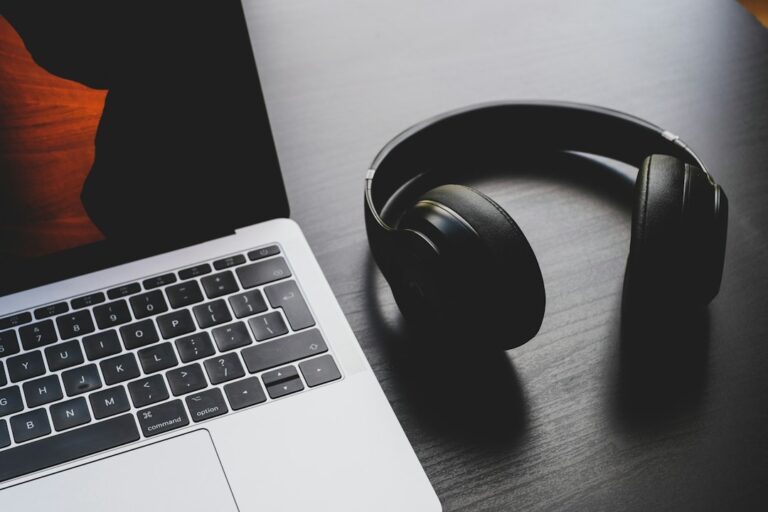 Black over-ear headphones beside a silver laptop on a wooden desk.