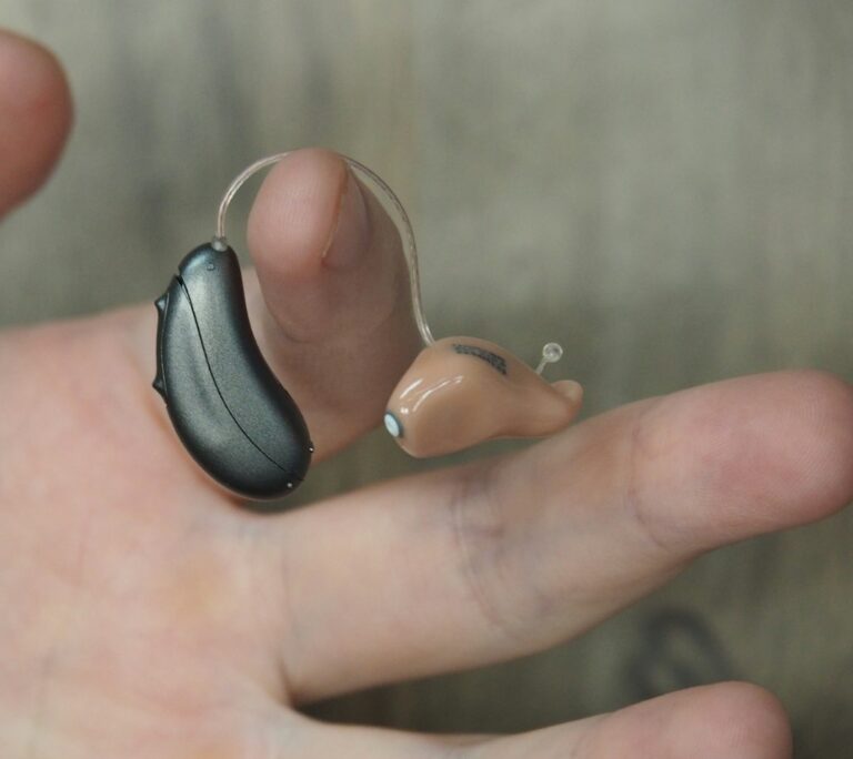 A small behind-the-ear hearing aid with its earpiece resting on an open hand.