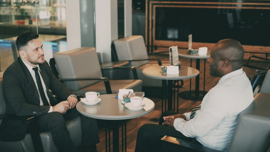 Two men seated across a café table during a conversation.