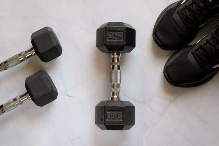 Black dumbbells and a pair of black sports shoes on a light floor.