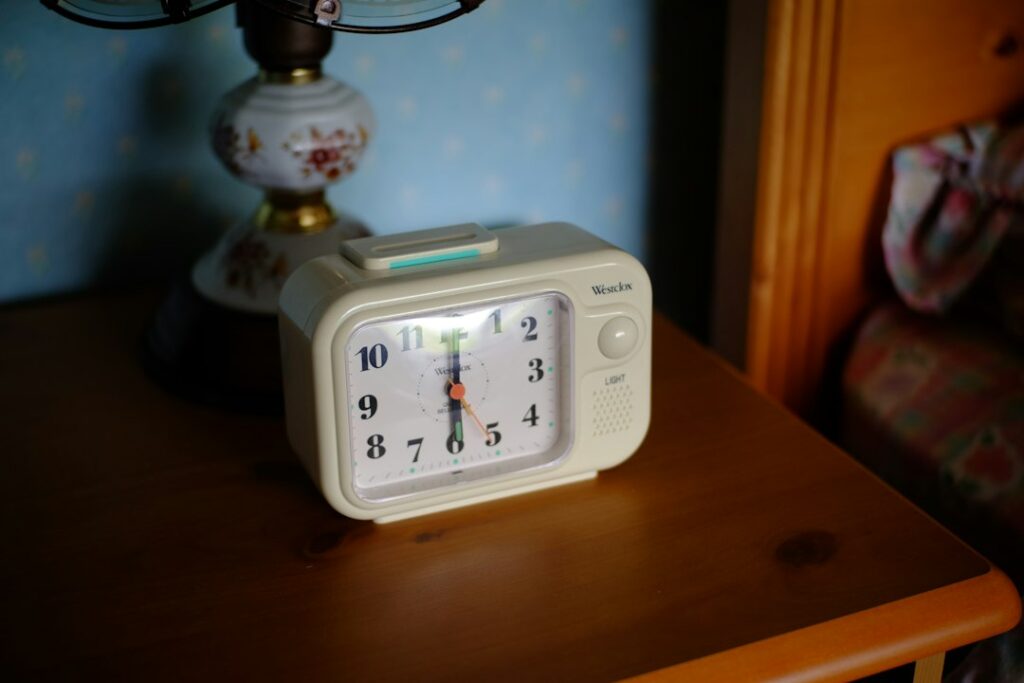 An analog alarm clock on a wooden bedside table.