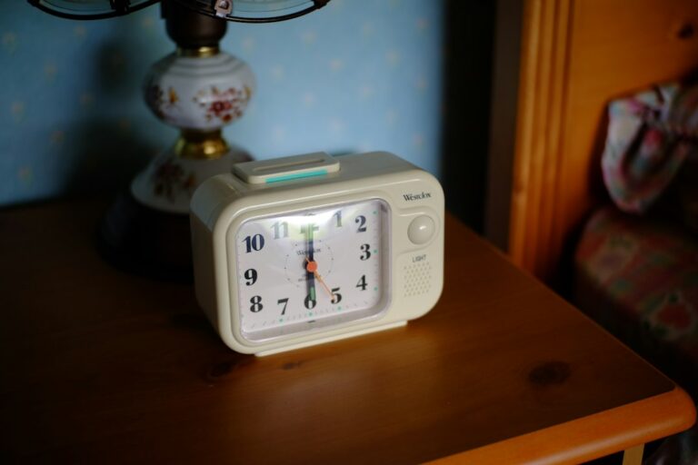 An analog alarm clock on a wooden bedside table.