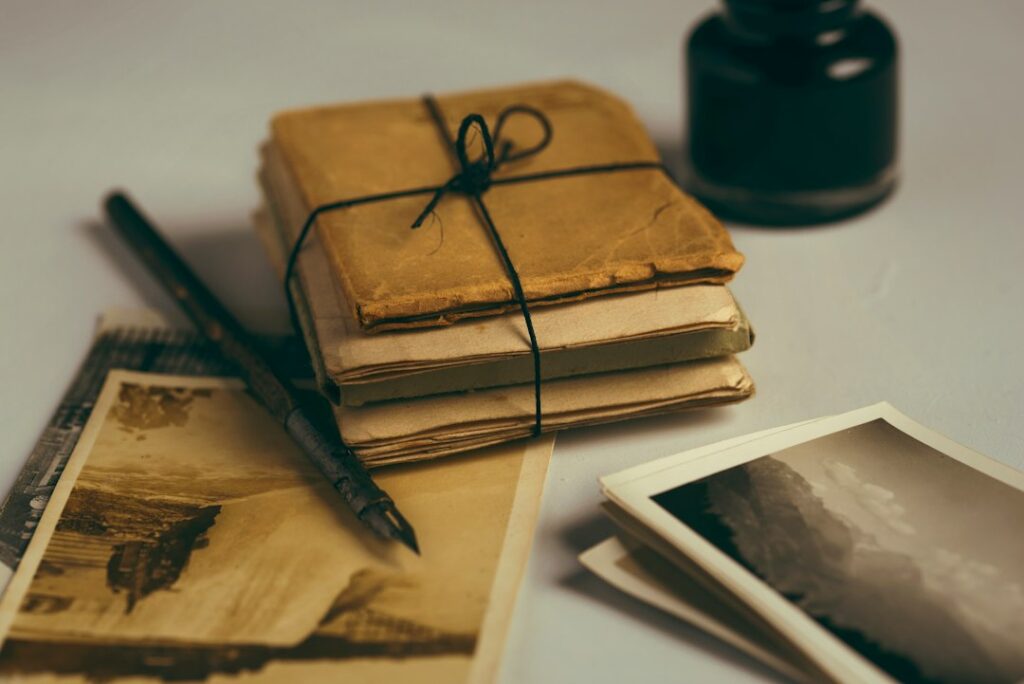 Old notebooks tied with string beside a pen, ink bottle, and photographs.