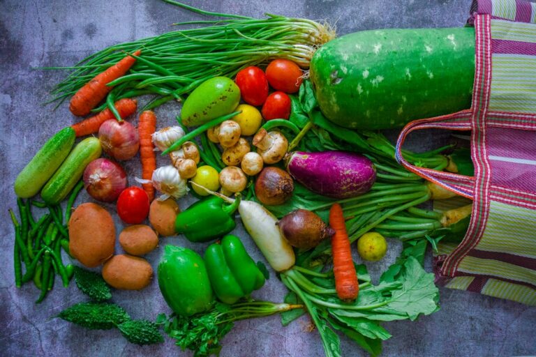 Fresh vegetables spread beside a reusable striped shopping bag.