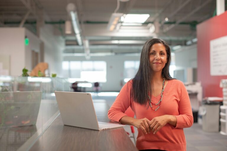 A woman standing beside an open laptop in an office.