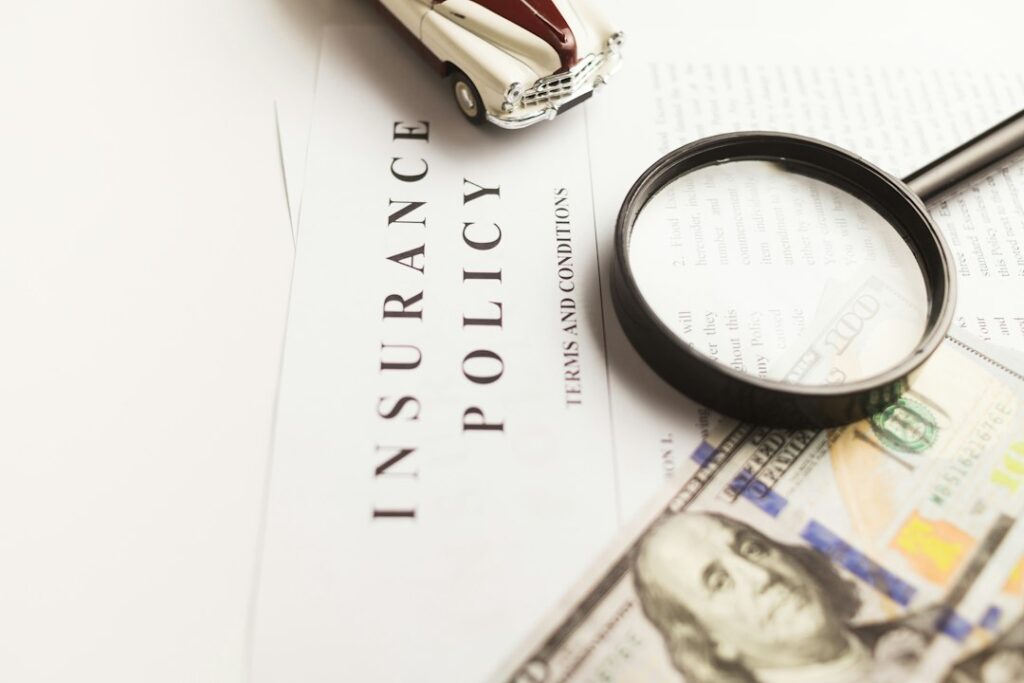 A magnifying glass, model car, and banknotes arranged over an insurance document.