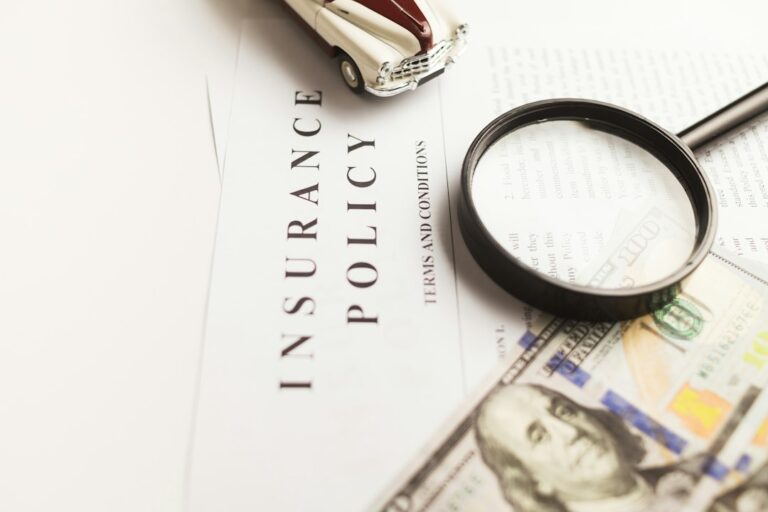 A magnifying glass, model car, and banknotes arranged over an insurance document.