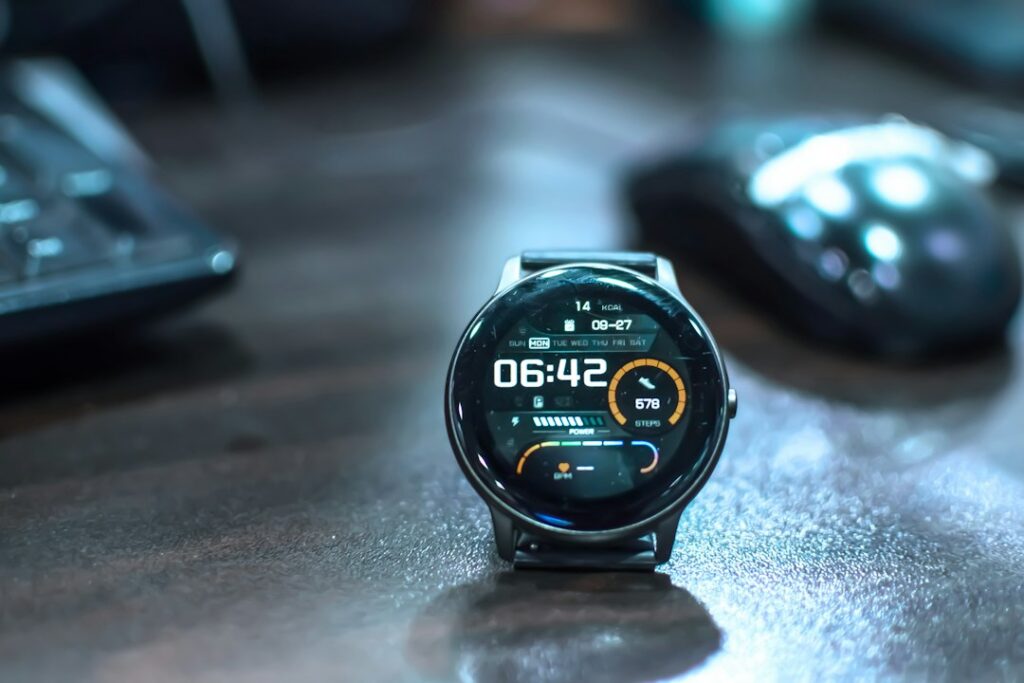 Round smartwatch resting on a desk beside a keyboard and mouse.