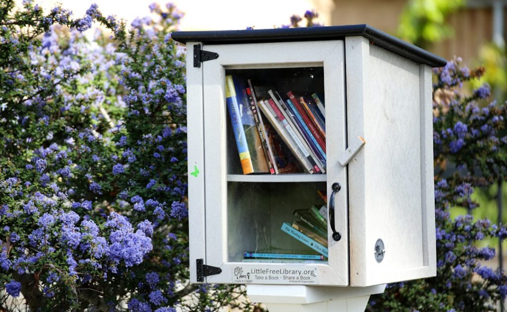 A neighborhood book-sharing cabinet surrounded by flowering shrubs.
