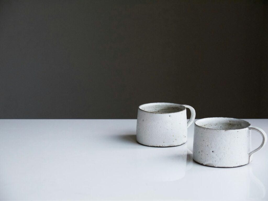Two white handmade ceramic cups on a light-colored tabletop.