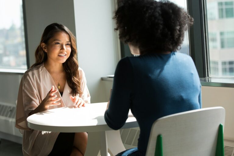Two people talking across a table during a meeting.