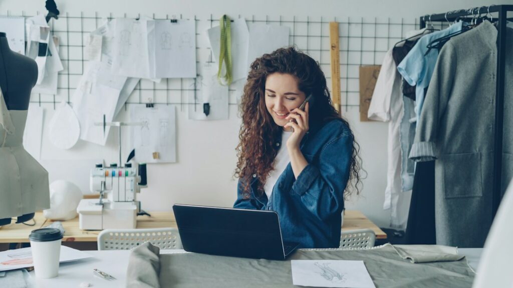 A person using a laptop and phone at a desk in a clothing shop.