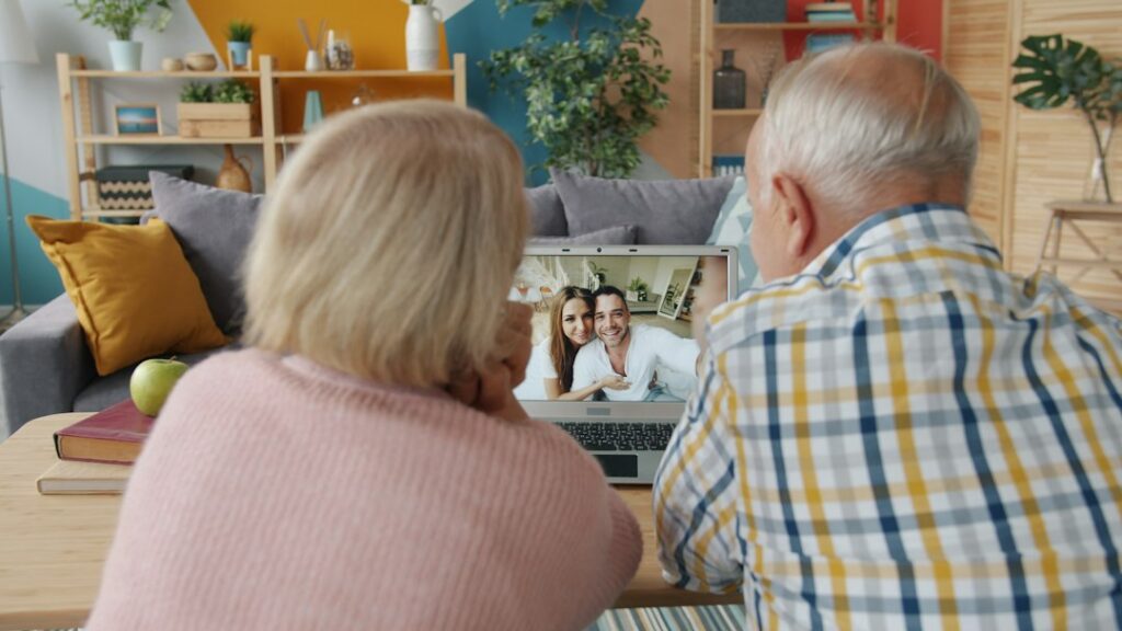 Two older adults talking with two people on a laptop video call at home.