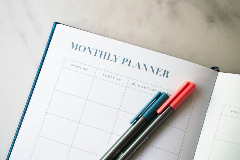 Two pens on an open monthly planner with empty calendar spaces.