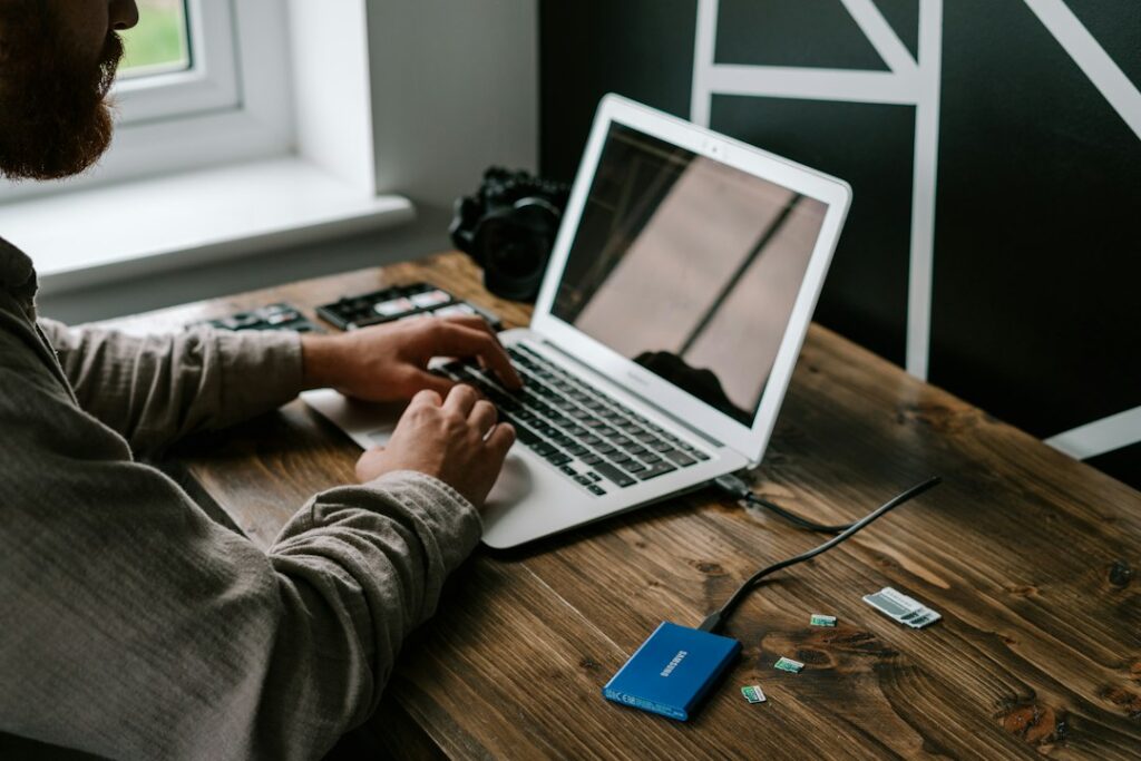 Hands using a laptop beside a portable external drive and memory cards.