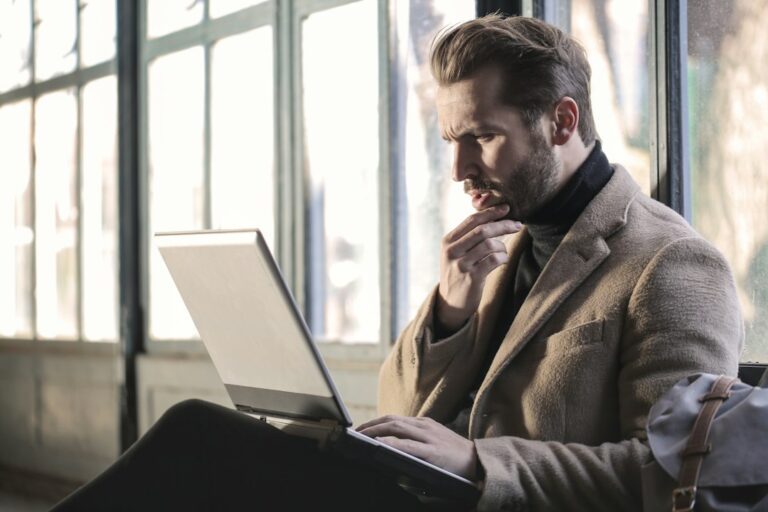 A man looking at a laptop with one hand resting on his chin.