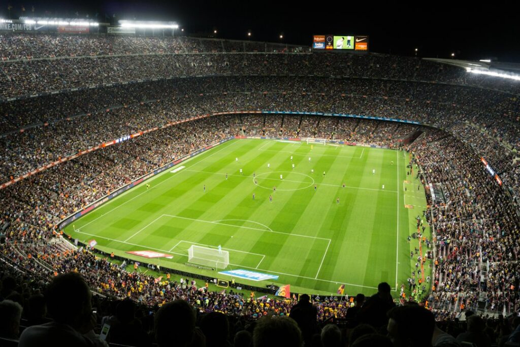 Spectators surrounding a floodlit soccer field during a match.