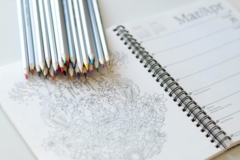Colored pencils resting on an open coloring book and planner.