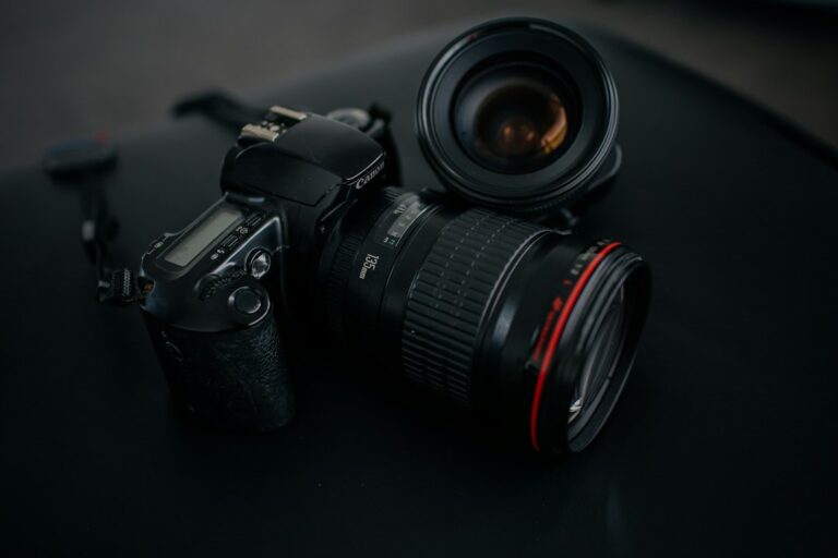 A camera with a telephoto lens beside another lens on a dark surface.