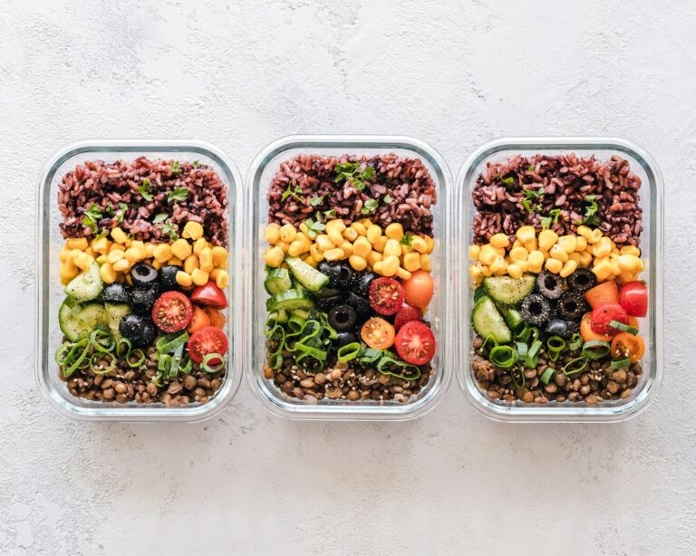 Three glass food containers filled with grains, legumes and colorful vegetables.