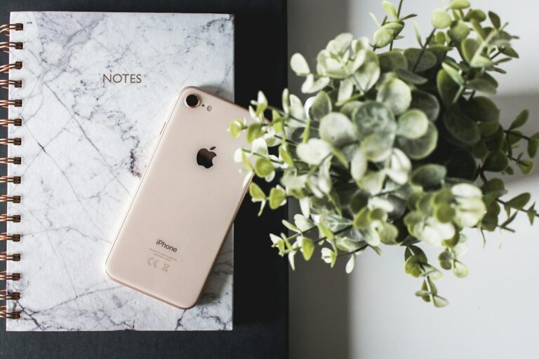 A smartphone resting on a notebook beside a green plant.