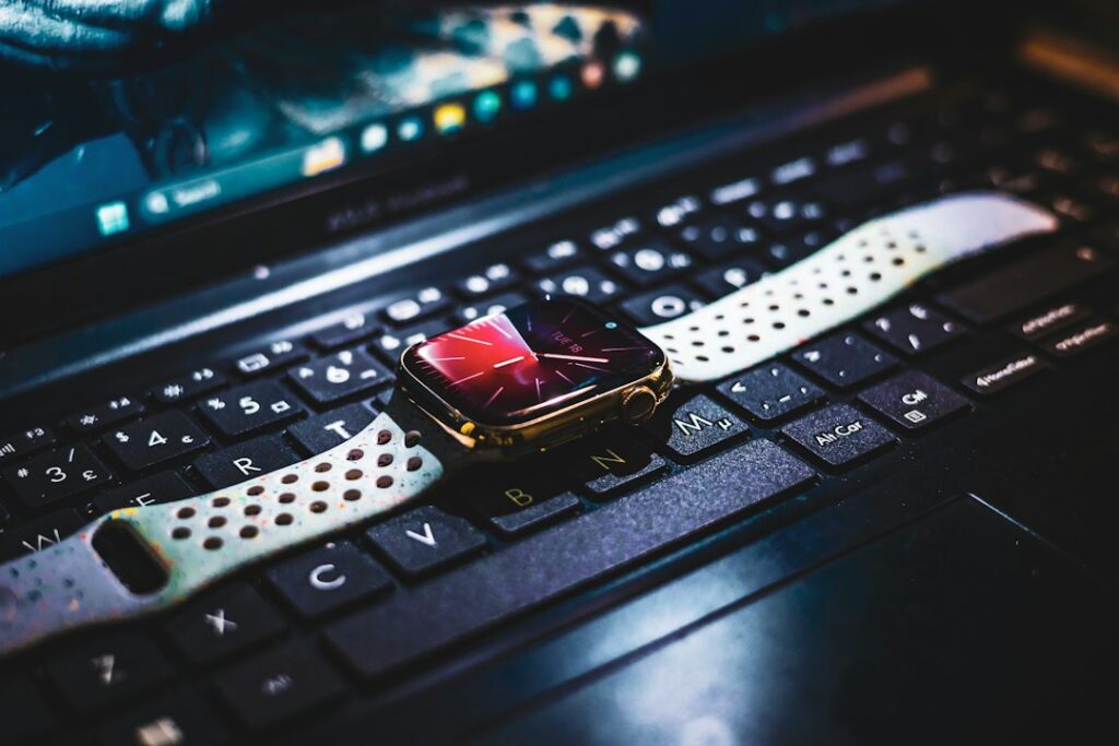 A smartwatch with a light-colored band resting on a laptop keyboard.